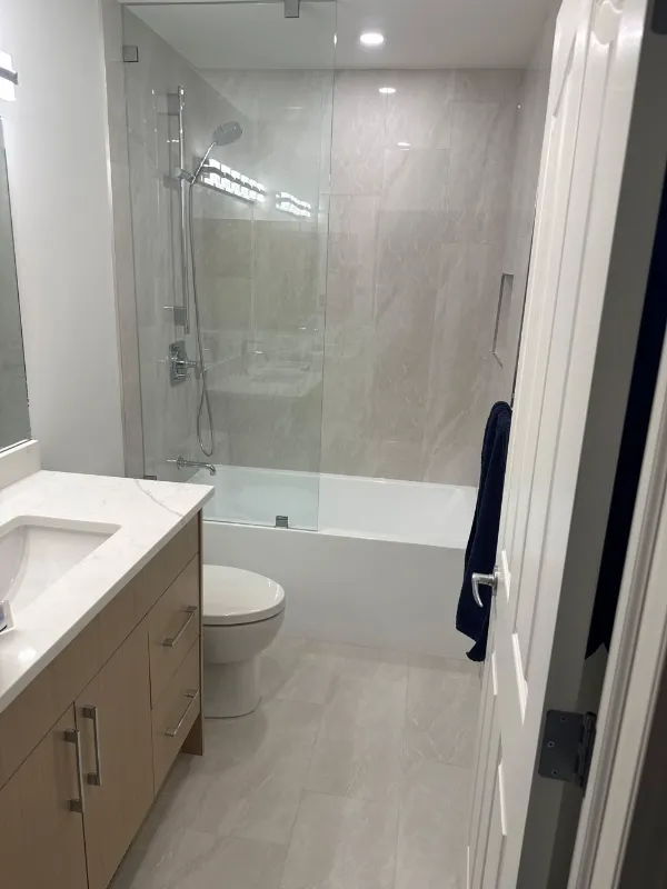 Bathroom renovation with glass tub-shower enclosure and wood vanity