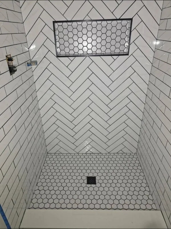 Walk-in shower with white herringbone subway tile and hexagon floor